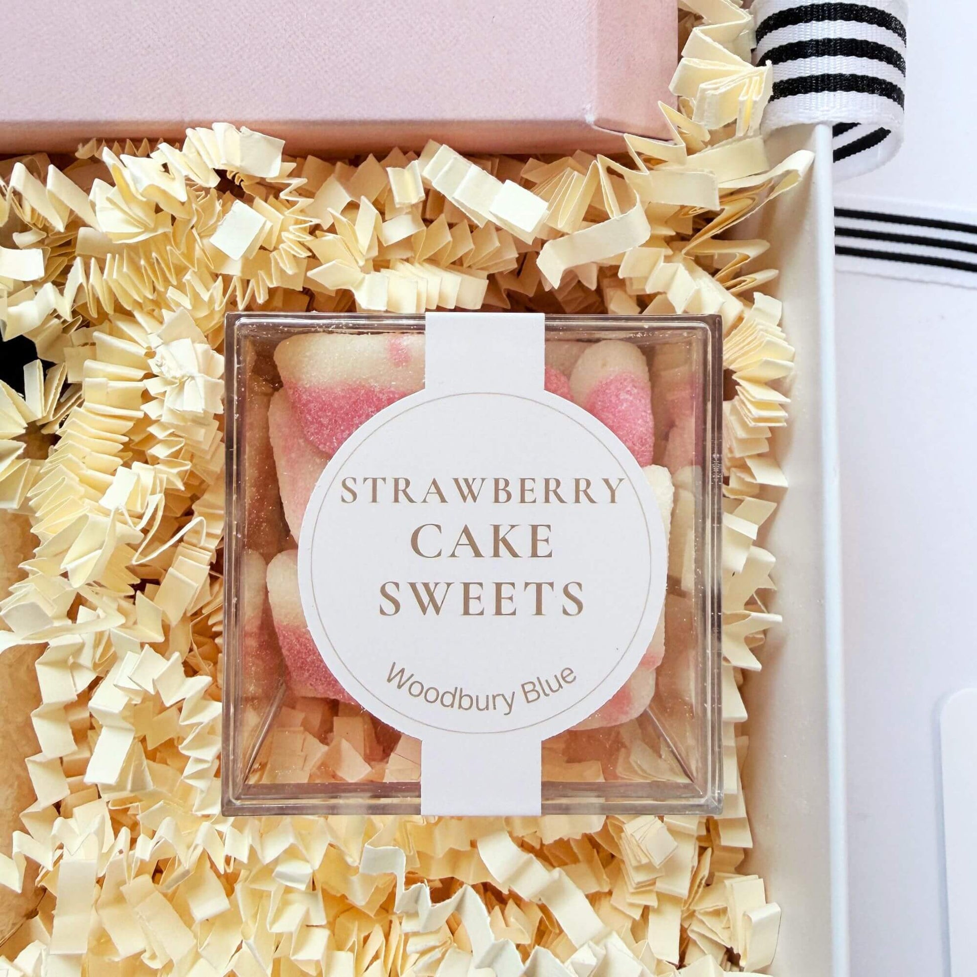 Strawberry cake sweets inside a luxury birthday gift box with cream shredded paper and ribbon.