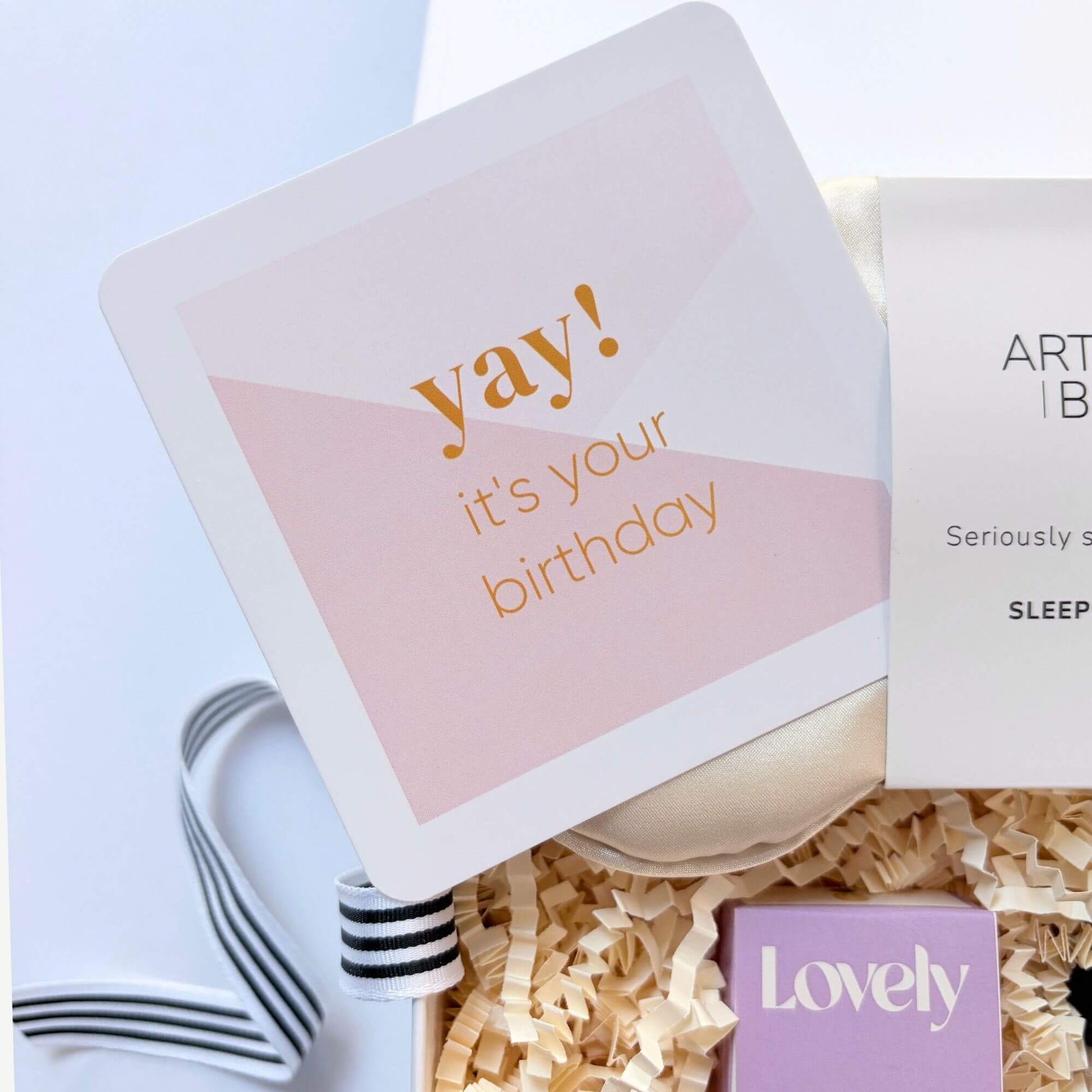 Pink birthday card inside a luxury birthday pamper gift box with silk eye mask and pineapple coconut lip balm.