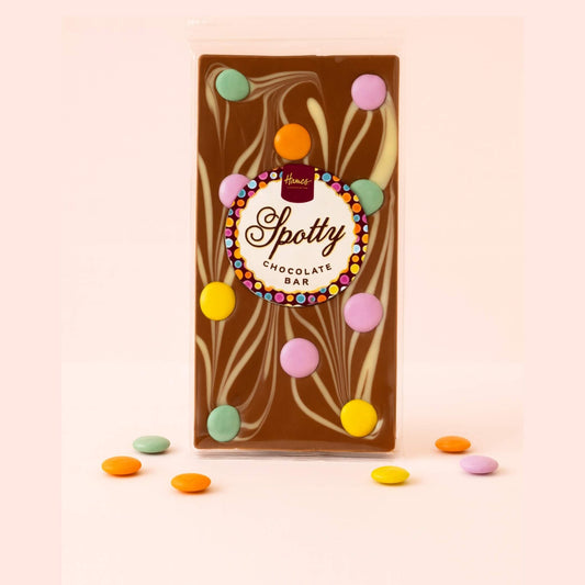 Chocolate bar with colorful candy pieces on a light pink background