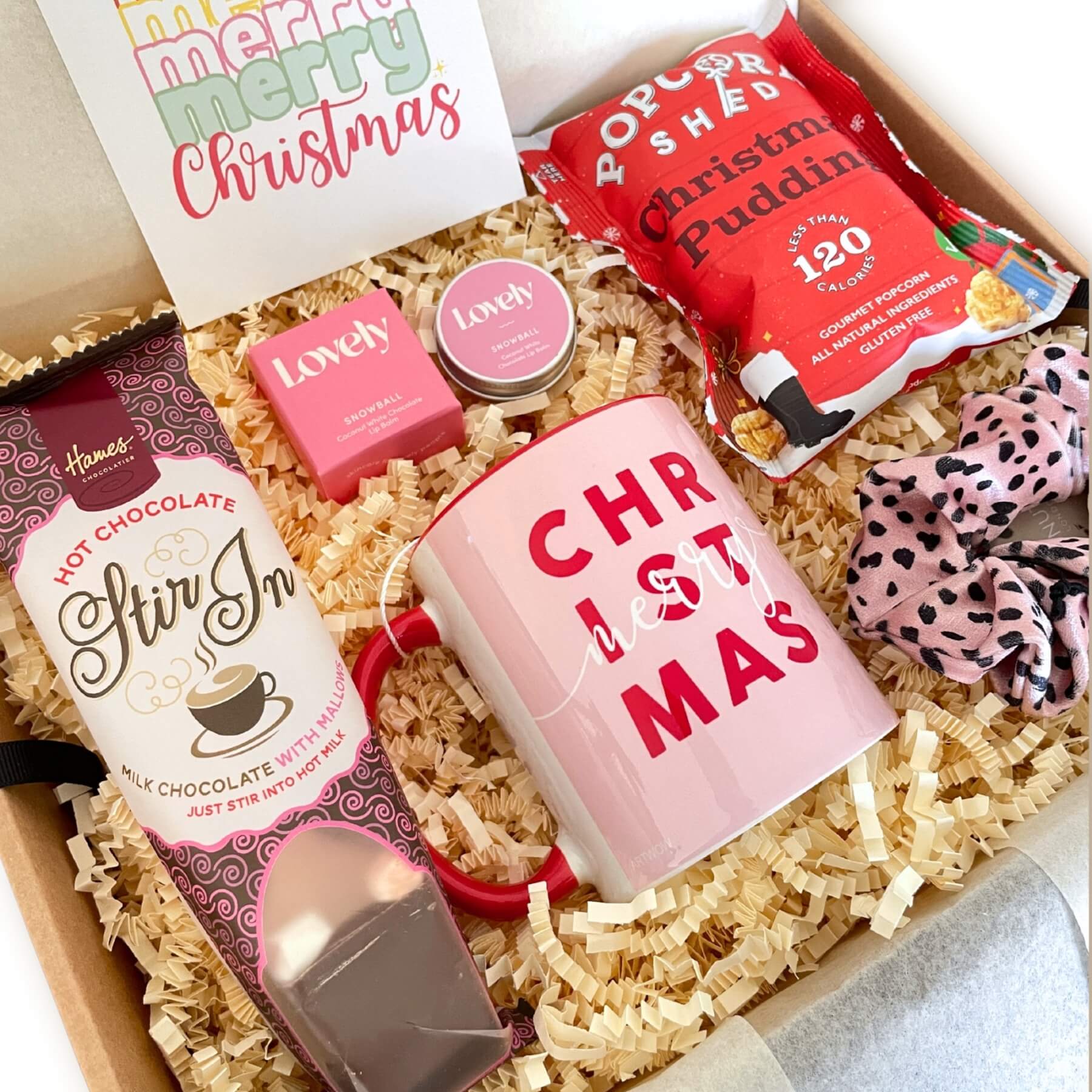 Close up of the Merry Christmas Gift Box with pink Christmas mug, hot chocolate stir in, popcorn and Lovely Snowball skincare treats.