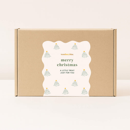 Kraft gift box with scalloped white Merry Christmas sticker decorated with small Christmas trees from Woodbury Blue