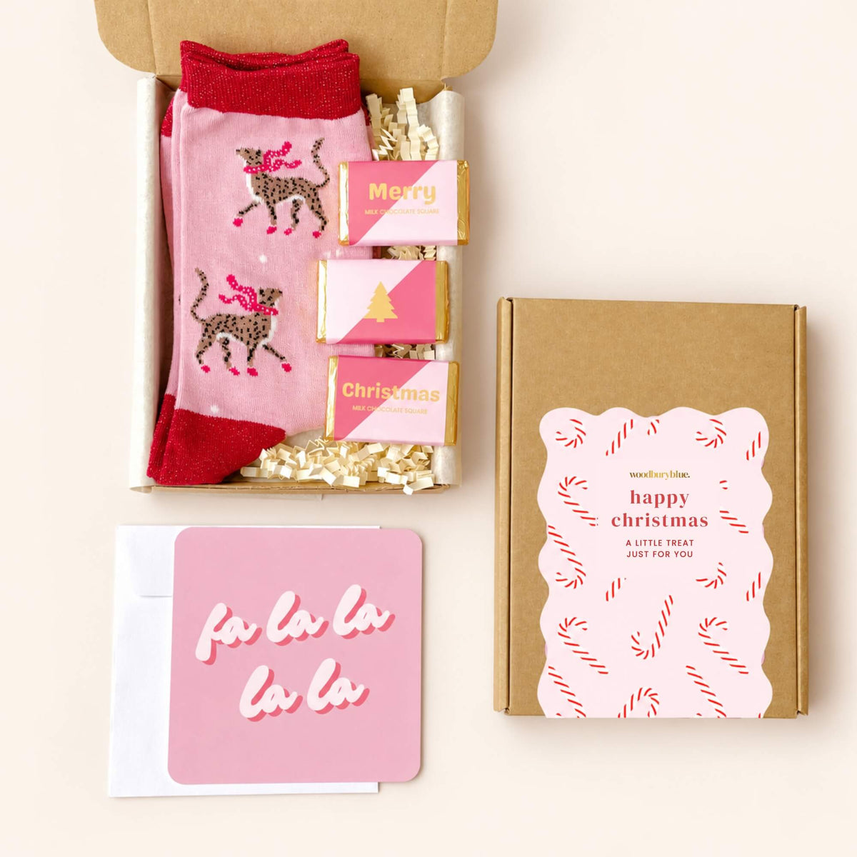 Open Christmas letterbox gift containing pink cheetah socks and three mini milk chocolates, with a Fa La La card, envelope and gift box beside it.