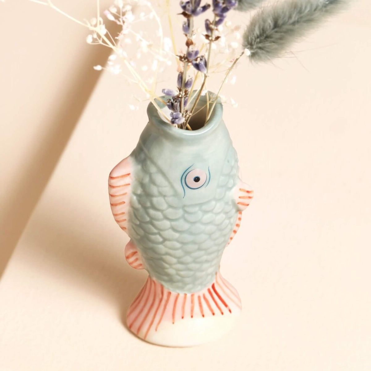 Close-up of a blue and pink ceramic fish bud vase showing the raised scales, eye detail, pink fins and opening for dried stems.