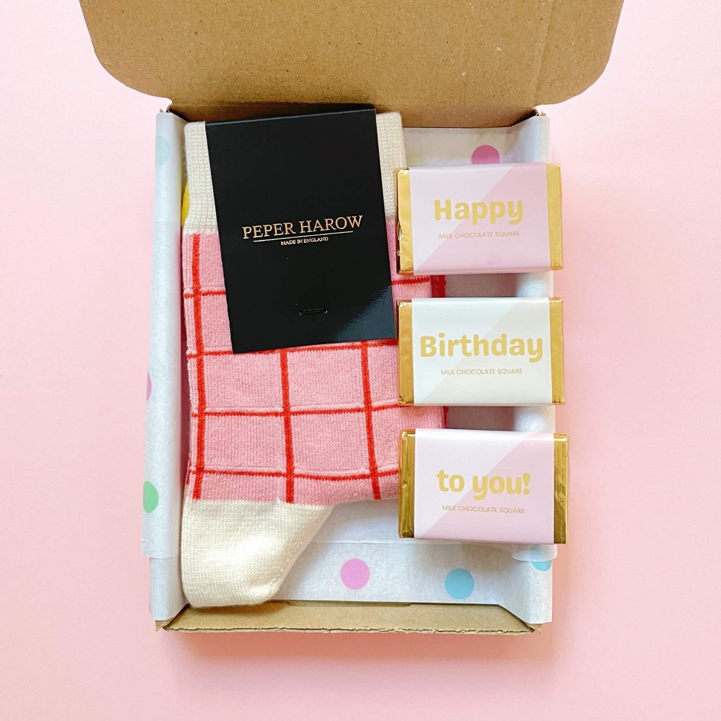 Open birthday letterbox gift with pink and cream grid socks and three chocolate squares by Woodbury Blue.
