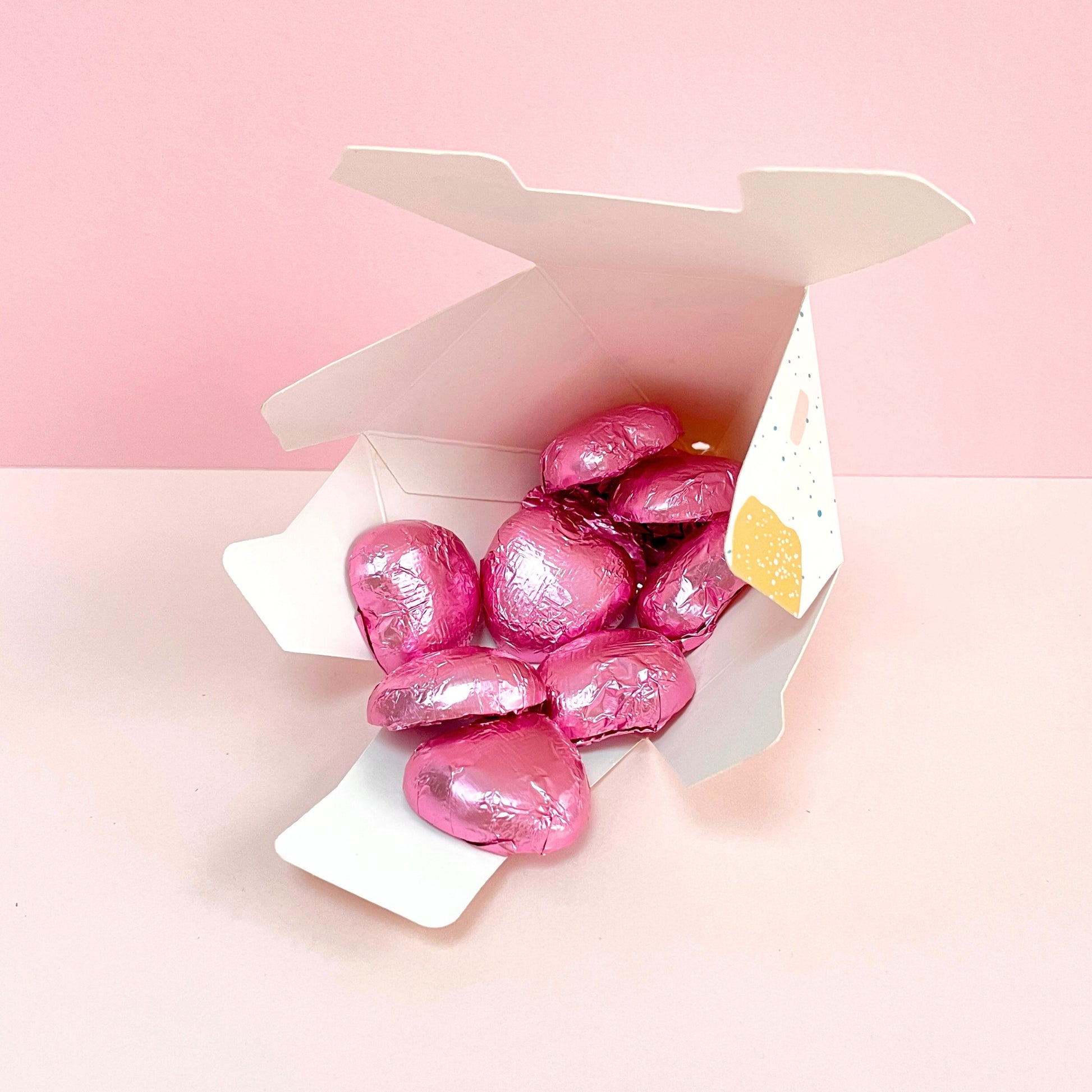 Open gift box filled with pink foiled chocolate hearts