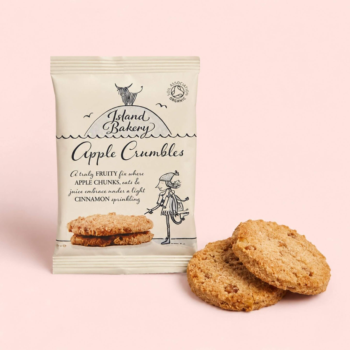 Island Bakery Organic Apple Crumble Biscuits with two biscuits beside the packet on a blush pink background.