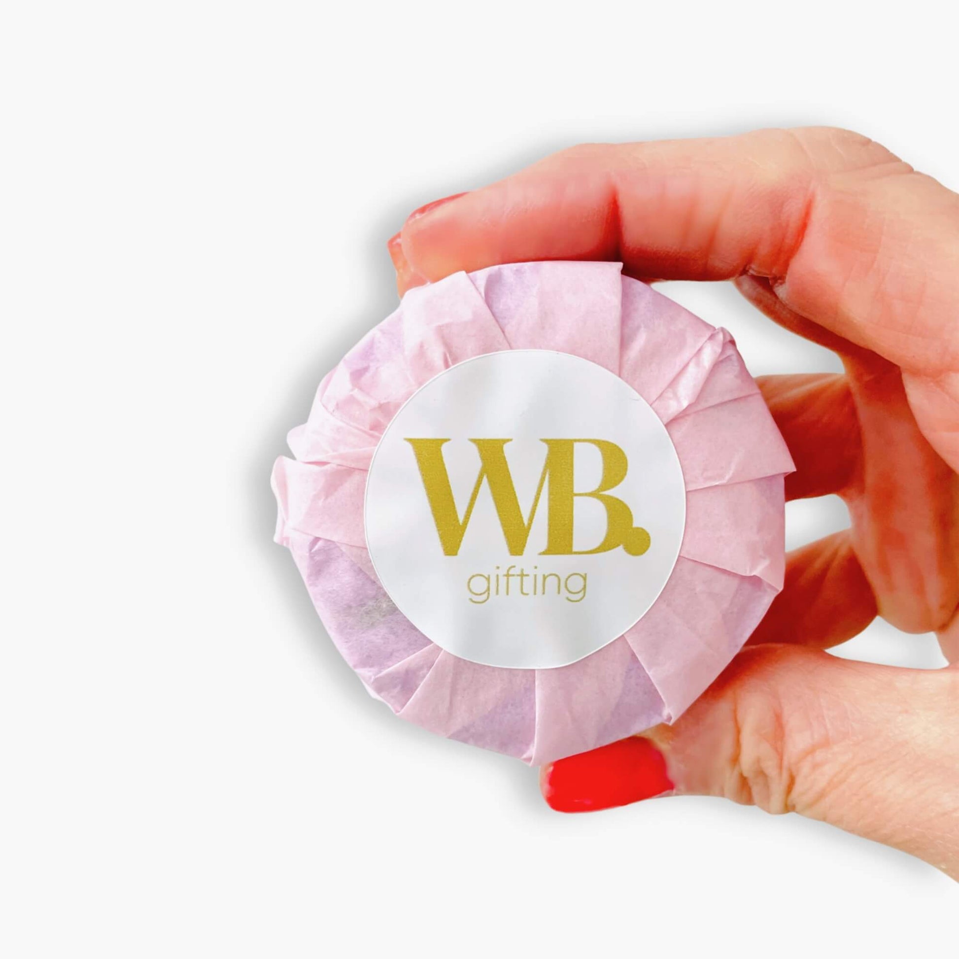 Hand holding a wrapped Woodbury Blue Tranquility shower steamer in pink tissue paper