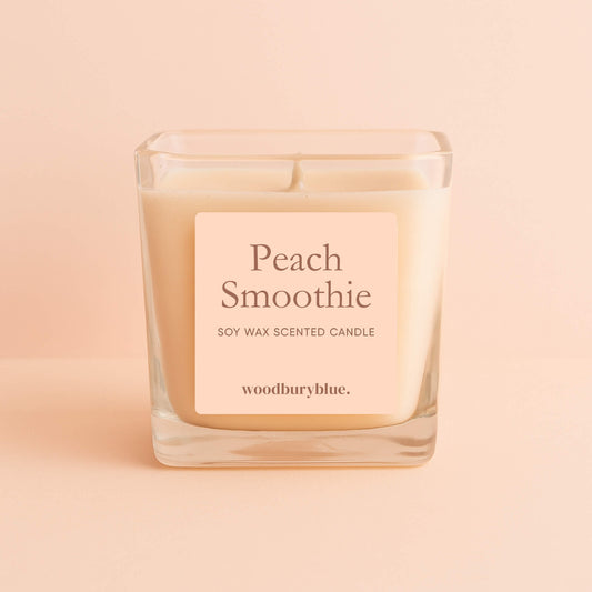 Peach Smoothie soy wax scented candle in a square glass jar with Woodbury Blue label, displayed on a soft peach background
