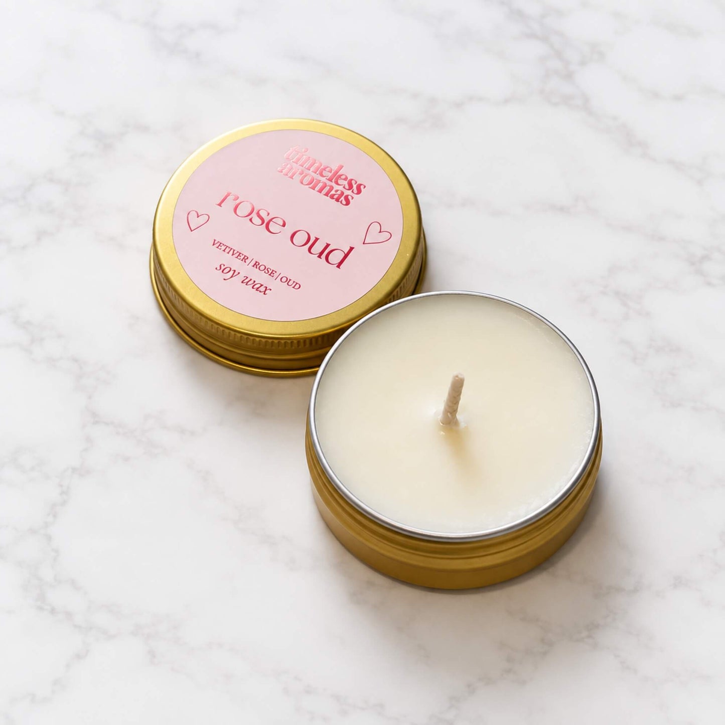 Open Rose Oud mini soy wax candle with gold tin lid on a light marble background