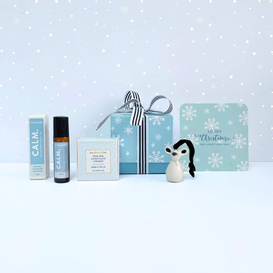Silent Night Christmas Gift Box with CALM pulse point roll-on, ceramic mouse ornament, pink gin chocolate creams, and snowflake notecard on a snowy background