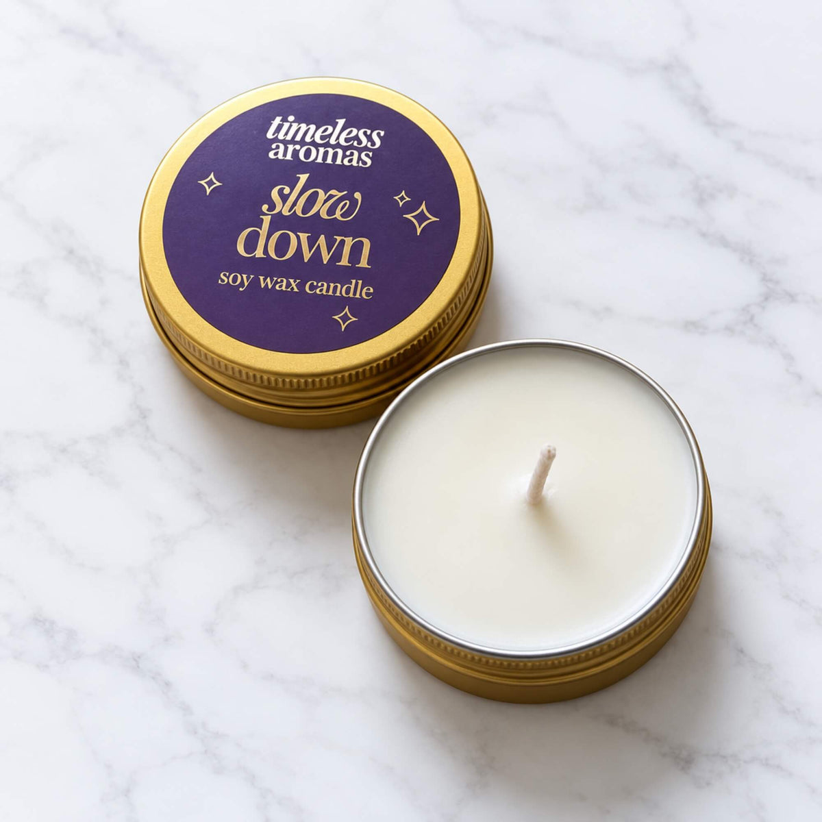 Open Slow Down mini soy wax candle with gold tin lid on a light marble background