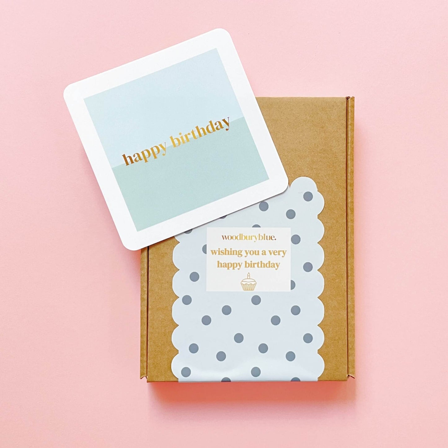 Woodbury Blue Socks and Chocs Letterbox Gift – Birthday Wishes, showing a brown gift box with polka dot sticker wrap and a pastel blue Happy Birthday card on a soft pink background.