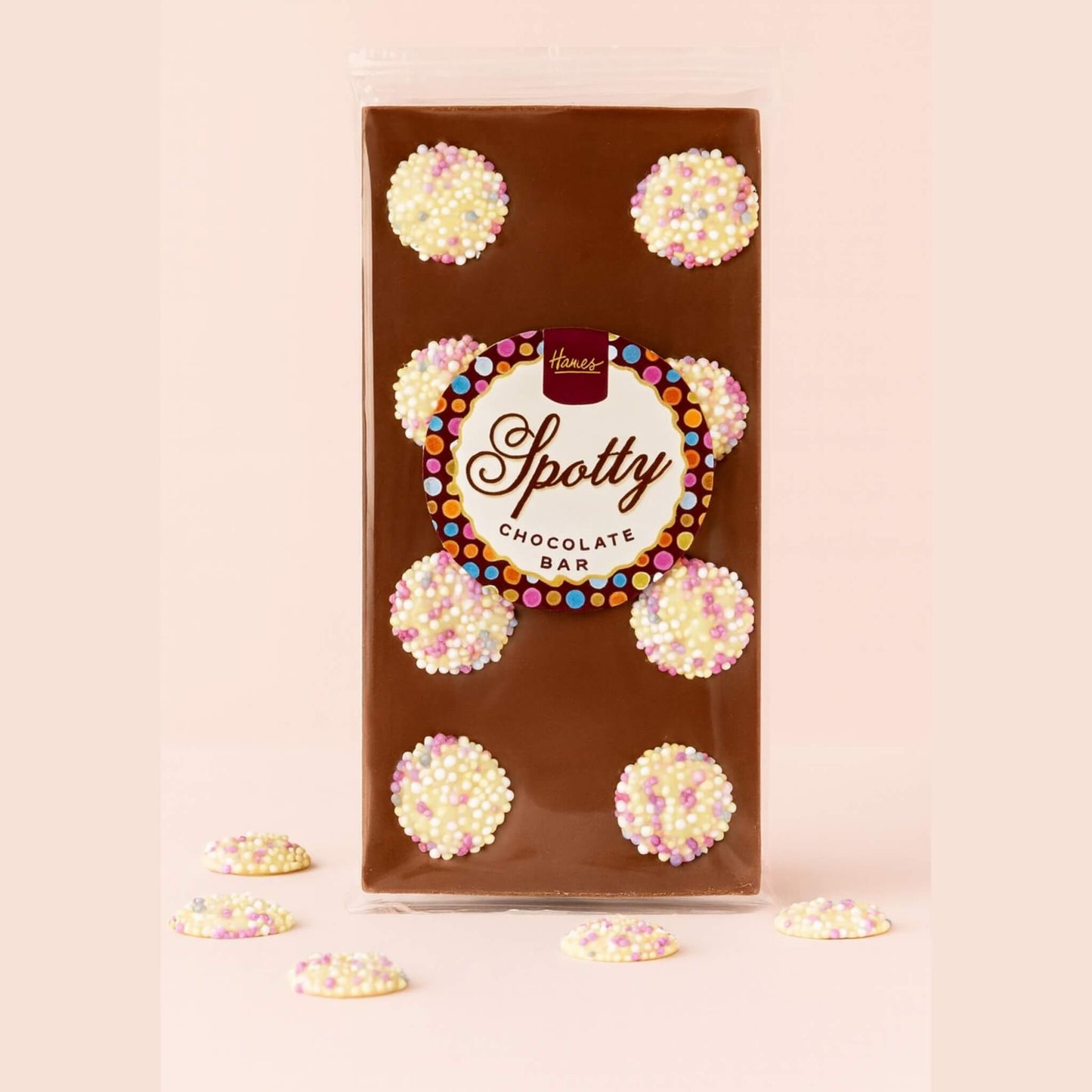 Hames Spotty milk chocolate bar decorated with white chocolate snowies on a soft blush pink background with snowies scattered around the base