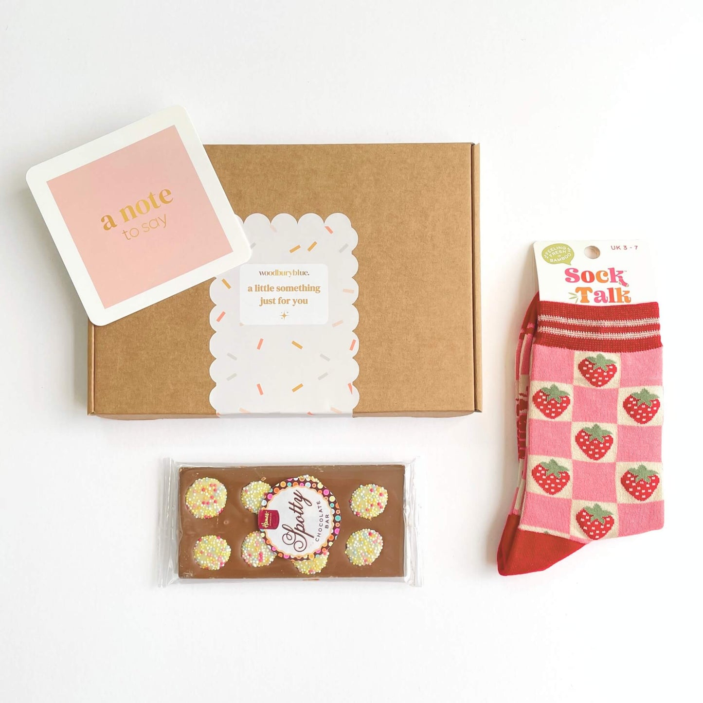 Flat lay of the Strawberry Dreams letterbox gift showing the gift box, strawberry socks, spotty chocolate bar and pink note card on a white background.