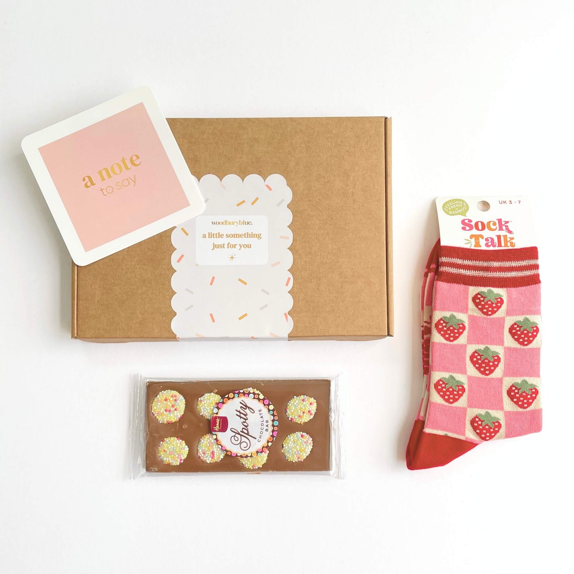 Flat lay of the Strawberry Dreams letterbox gift showing the gift box, strawberry socks, spotty chocolate bar and pink note card on a white background.