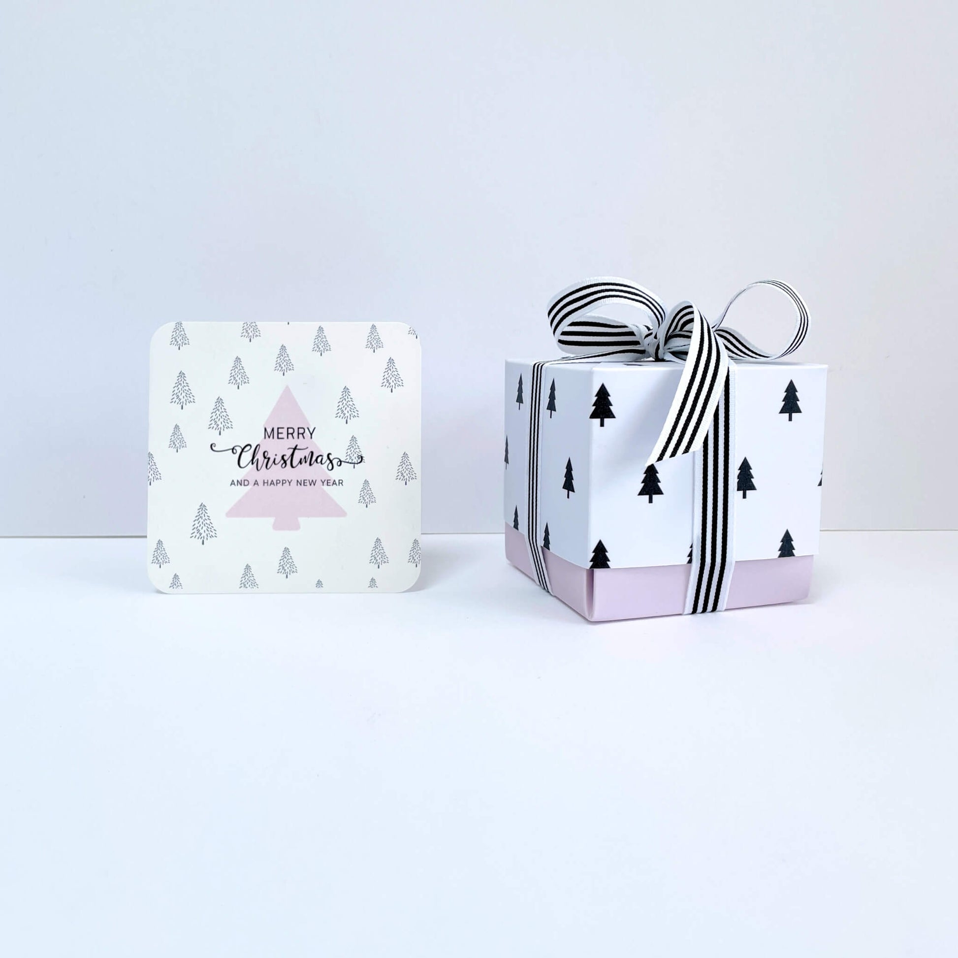 Merry Christmas notecard and white gift box with black tree design and striped ribbon