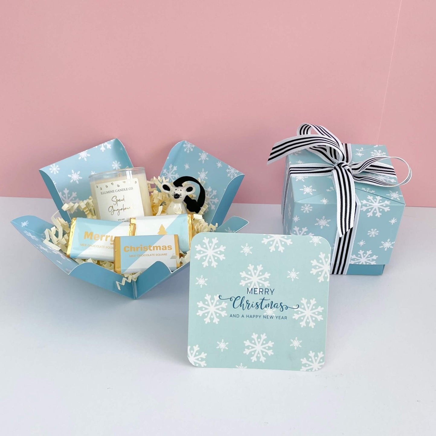  Winter Glow Gift Box both open and closed, styled with spiced gingerbread candle, mouse ornament, Merry Christmas card with snowflake print, and chocolate treats in a pale blue festive box.
