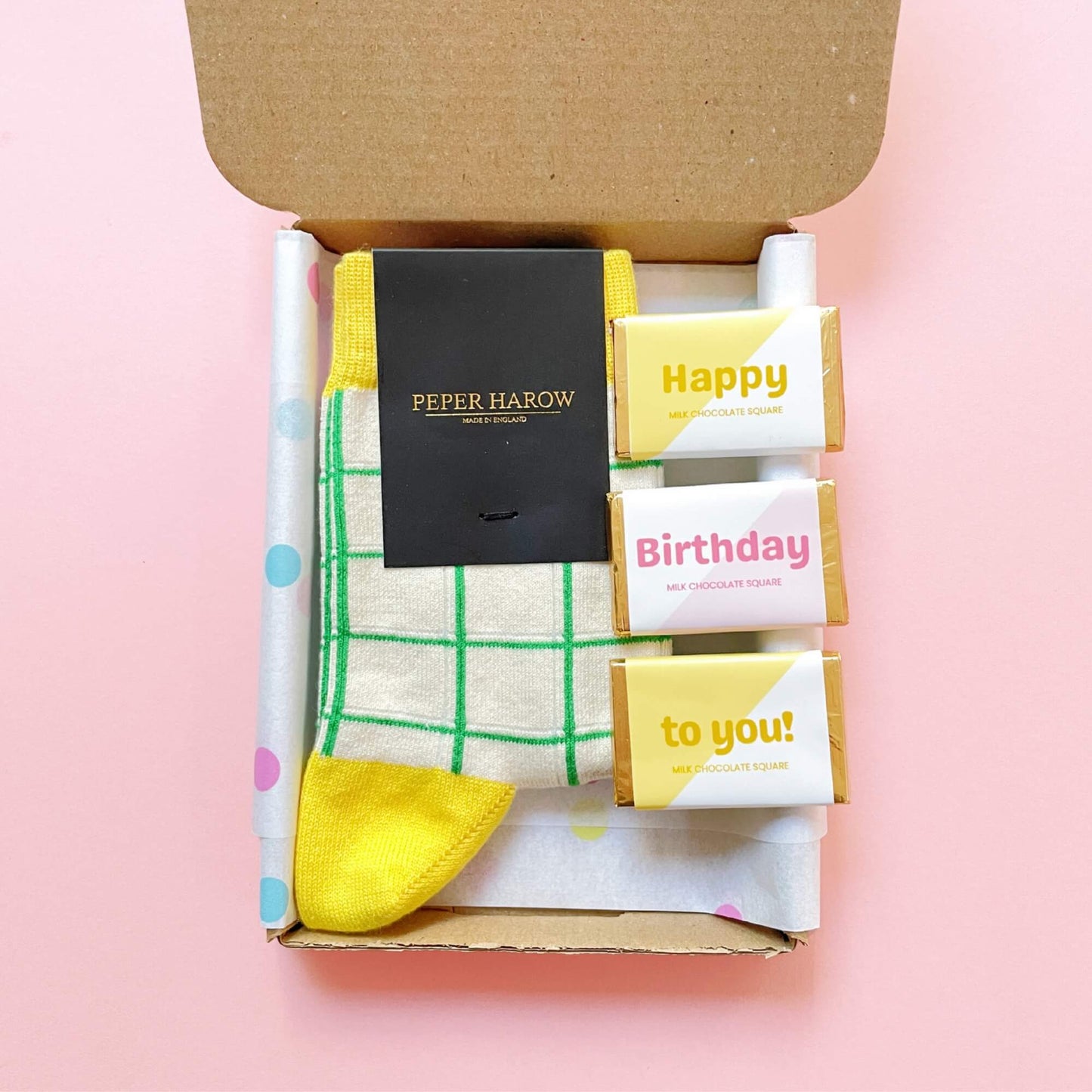 Open Woodbury Blue birthday gift box with yellow grid socks and Happy Birthday chocolate squares inside.