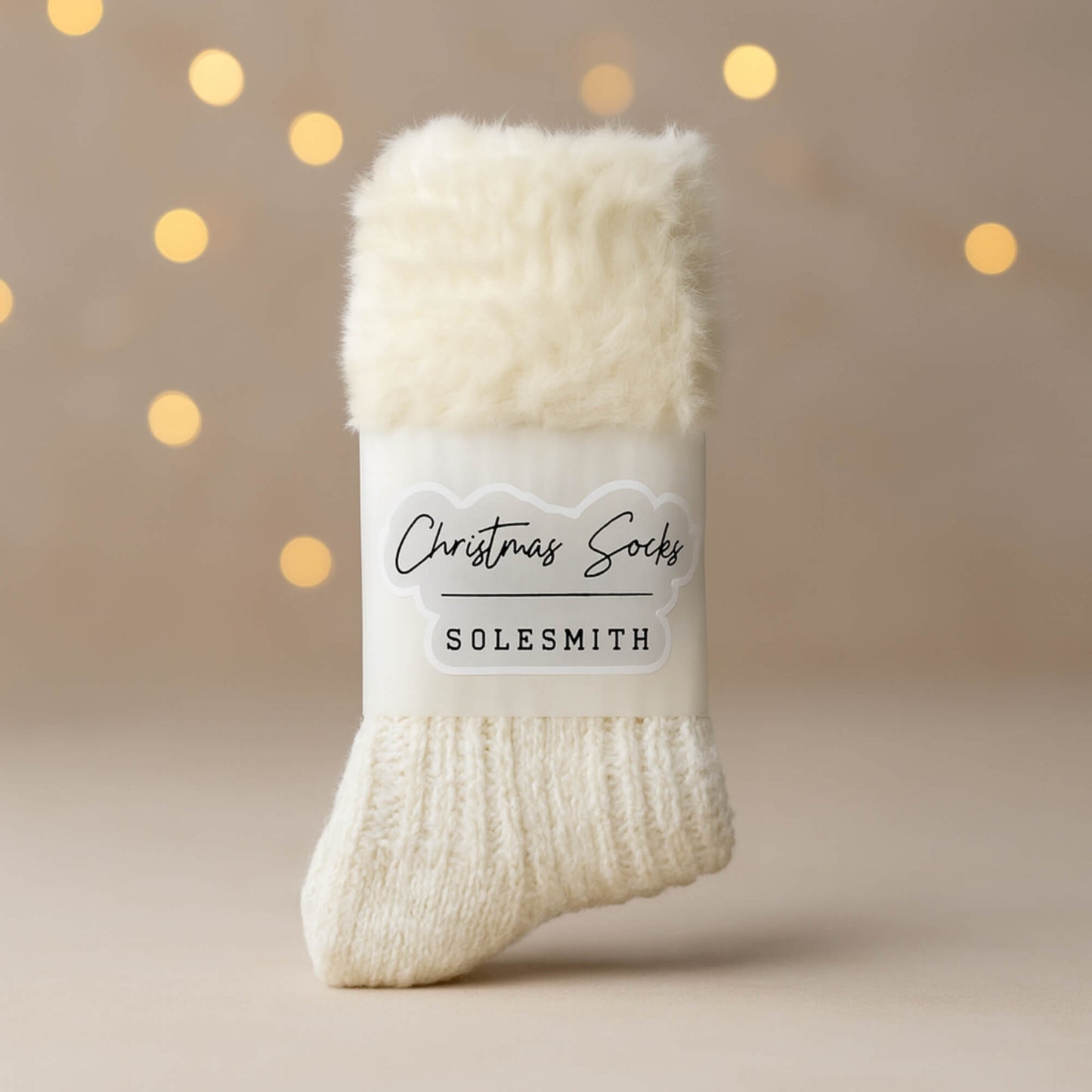 Cosy cream Christmas socks by Solesmith with a soft fluffy cuff, photographed on a neutral background with warm blurred fairy lights.