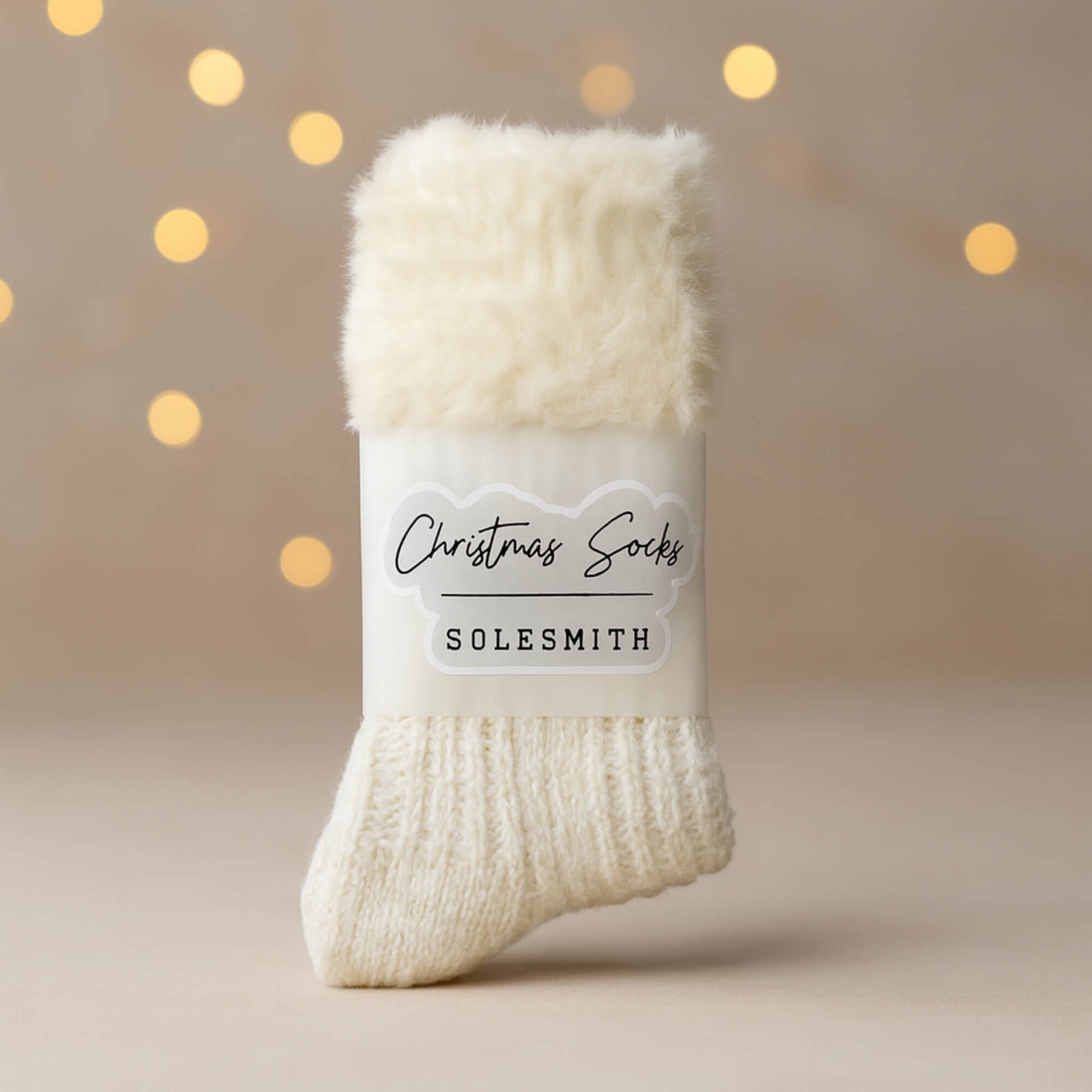 Cosy cream Christmas socks by Solesmith with a soft fluffy cuff, photographed on a neutral background with warm blurred fairy lights.