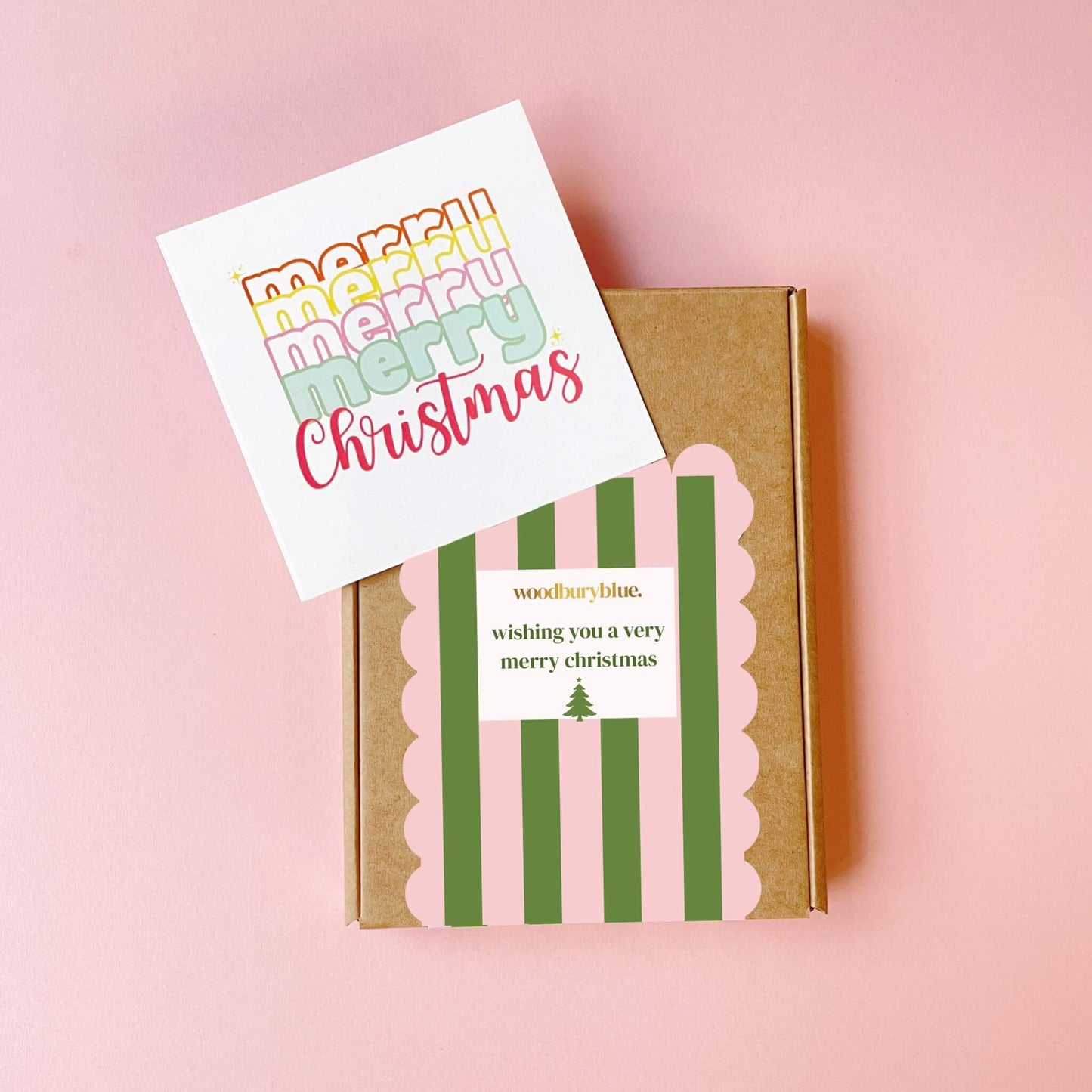 Closed Woodbury Blue Christmas gift box wrapped in pink and green striped packaging with notecard beside it