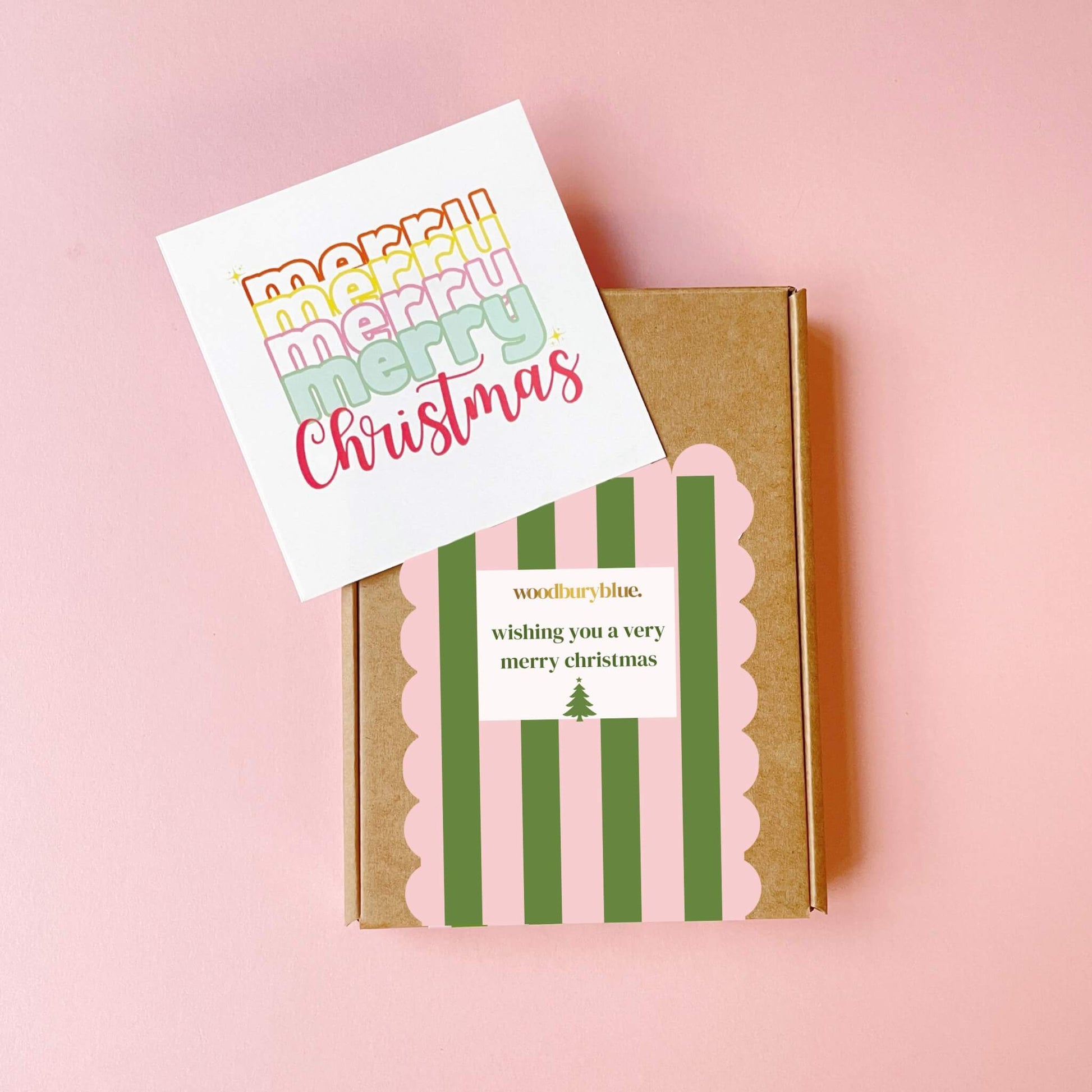 Closed Woodbury Blue Christmas gift box wrapped in pink and green striped packaging with notecard beside it
