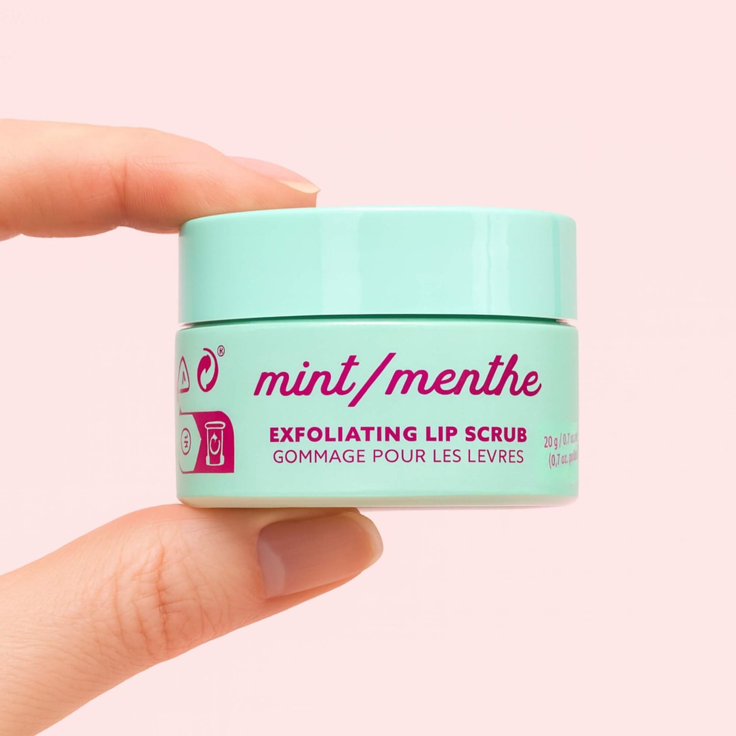 A mint green exfoliating lip scrub jar held between two fingers, showing the mint and menthe label in pink text.