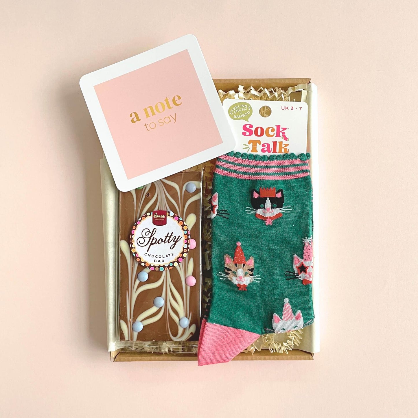 Close up of Party Cats bamboo socks and chocolate bar inside Woodbury Blue letterbox gift with pink background