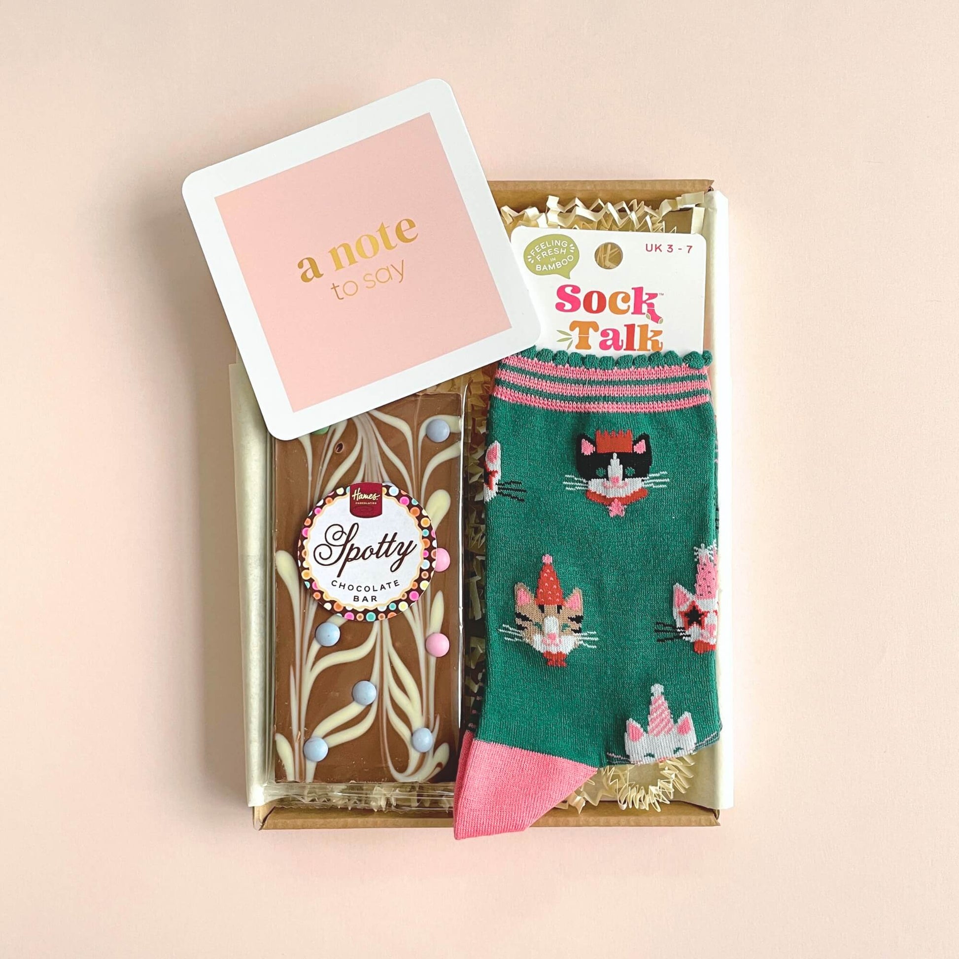 Close up of Party Cats bamboo socks and chocolate bar inside Woodbury Blue letterbox gift with pink background