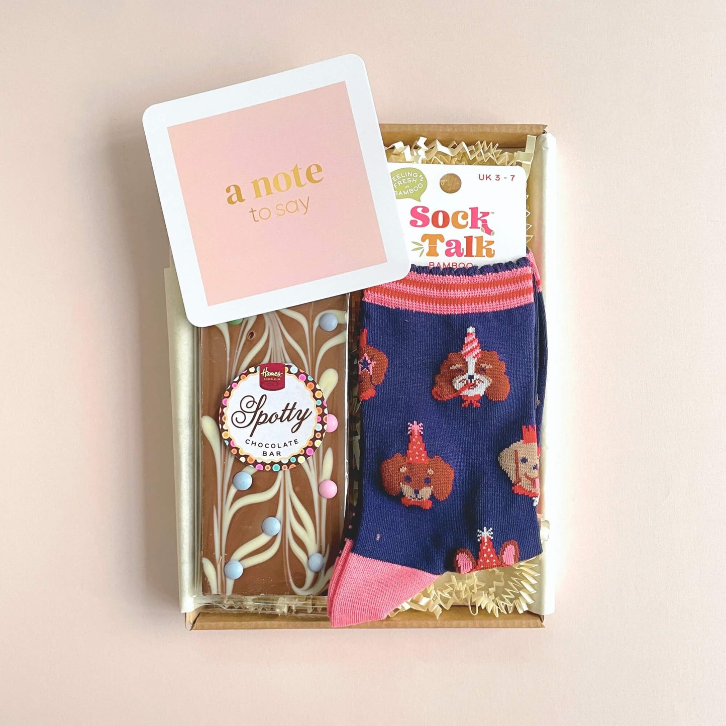 Close up of Party Dogs bamboo socks and artisan chocolate bar inside Woodbury Blue letterbox gift on pink background