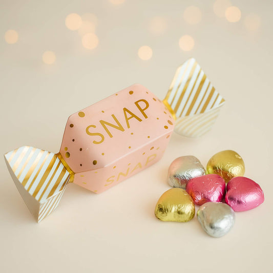 Pink and gold mini Christmas cracker with snap filled with foil-wrapped milk chocolate hearts by Woodbury Blue, styled on a soft neutral festive background.