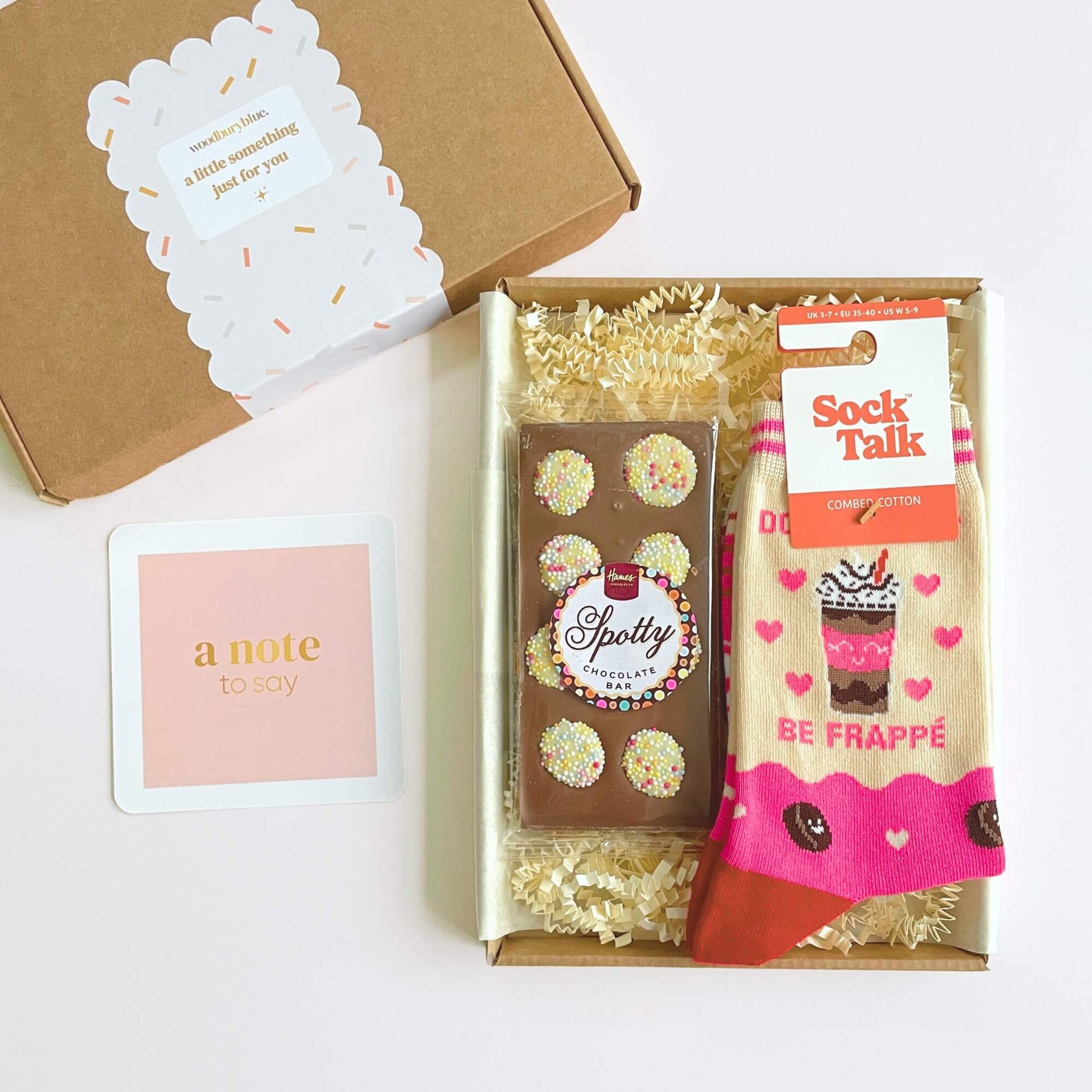 Coffee Lovers Socks and Chocs letterbox gift by Woodbury Blue, featuring a Spotty chocolate bar, Be Frappe socks and a note card arranged in a kraft gift box with shred.