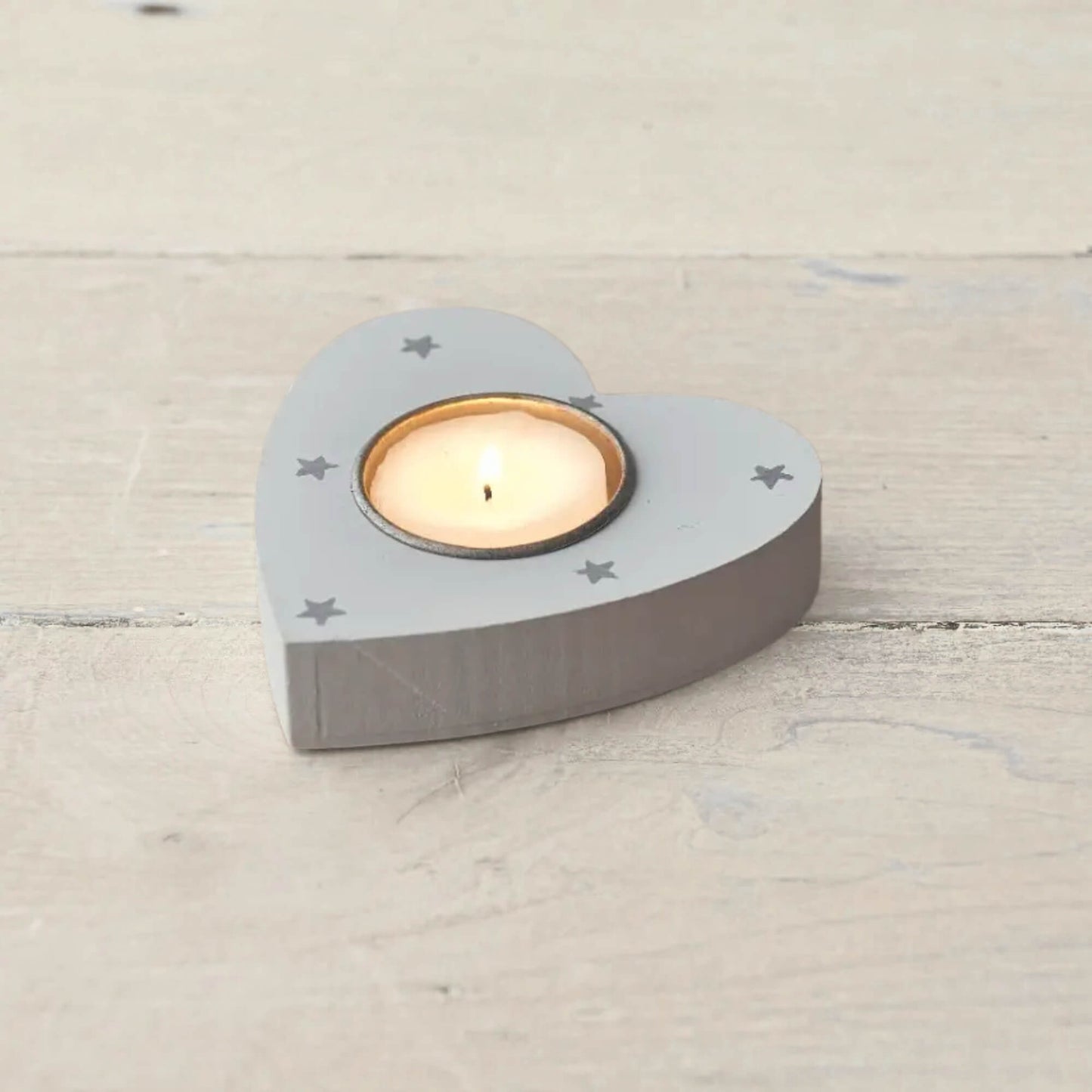 Grey wooden heart-shaped tea light holder with star design and lit candle on wooden surface