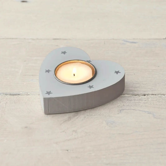 Grey wooden heart-shaped tea light holder with star design and lit candle on wooden surface