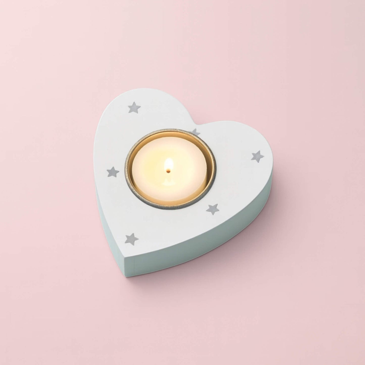 White wooden heart-shaped tea light holder with grey star pattern and glowing tealight on pink background
