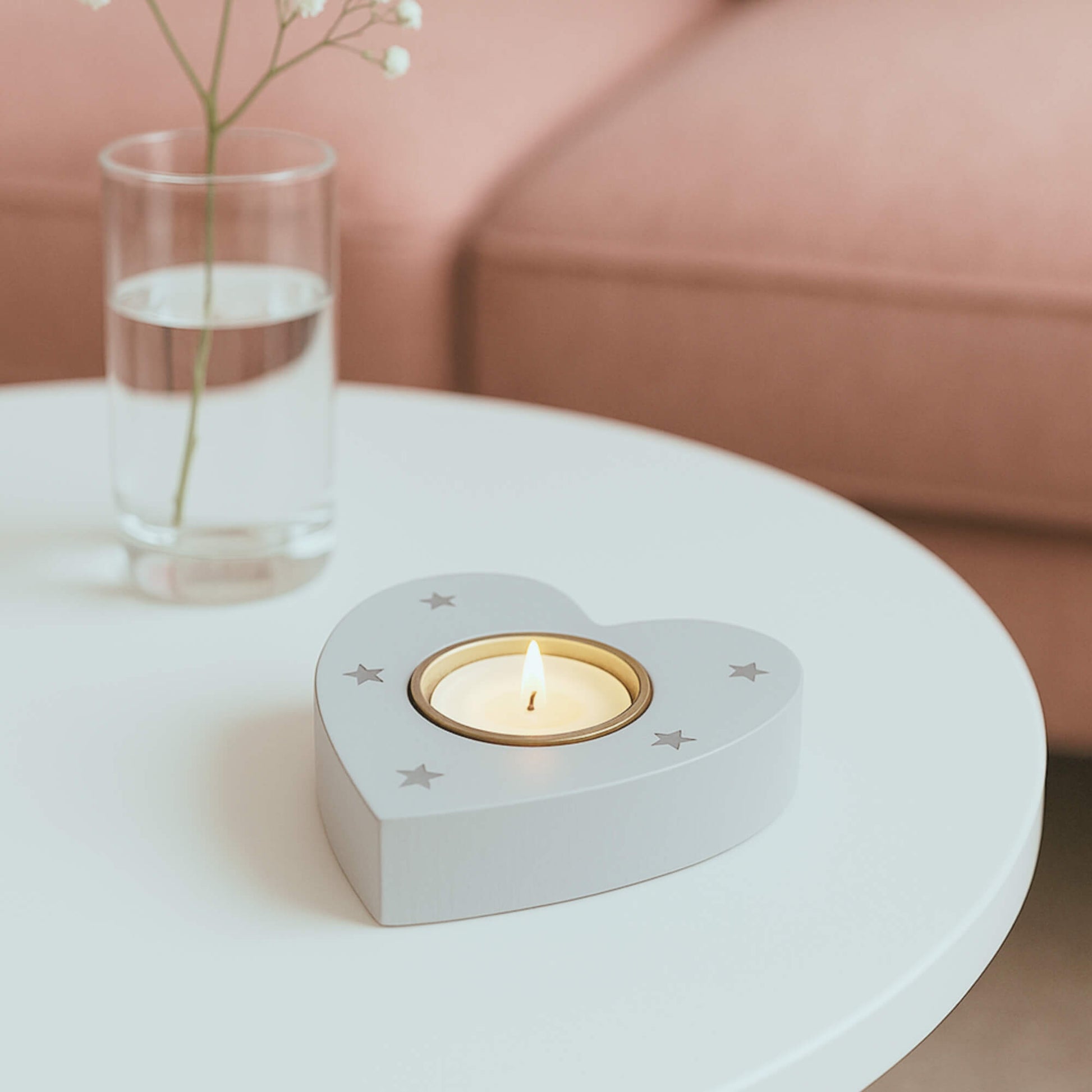 Heart-shaped wooden tealight holder with star design on white table, lit candle glowing with pink sofa in background